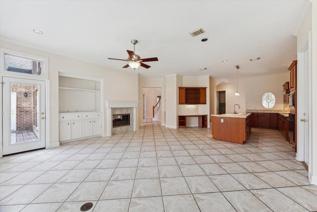 unfurnished living room with ceiling fan, built in shelves, light tile patterned floors, a high end fireplace, and sink