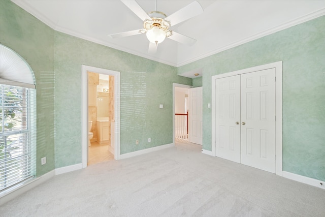 unfurnished bedroom featuring ceiling fan, crown molding, connected bathroom, carpet, and a closet