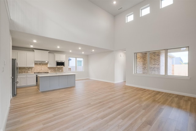 kitchen with a high ceiling, an island with sink, stainless steel appliances, light hardwood / wood-style floors, and decorative backsplash