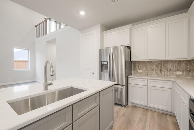 kitchen with white cabinets, stainless steel fridge, sink, light hardwood / wood-style flooring, and backsplash