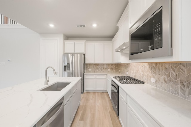 kitchen featuring sink, white cabinets, light stone counters, light wood-type flooring, and appliances with stainless steel finishes