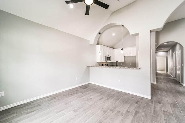 kitchen with light stone countertops, ceiling fan, kitchen peninsula, white cabinets, and light wood-type flooring