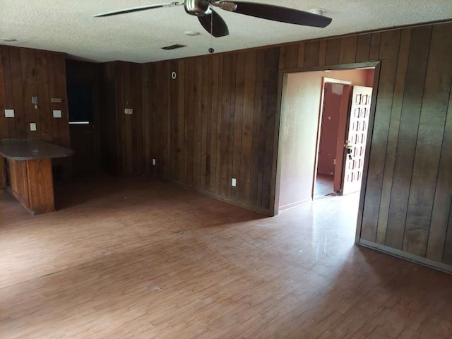 kitchen featuring ceiling fan, wooden walls, light hardwood / wood-style floors, and a textured ceiling