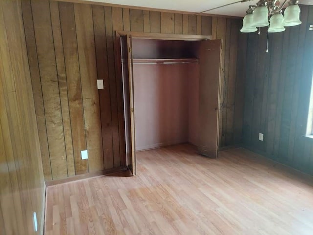 unfurnished bedroom featuring light wood-type flooring, wood walls, an inviting chandelier, and a closet