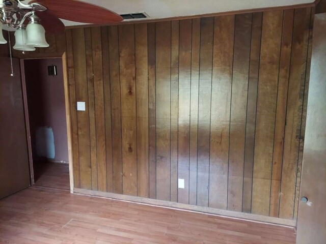 empty room with ceiling fan, wood walls, and hardwood / wood-style floors