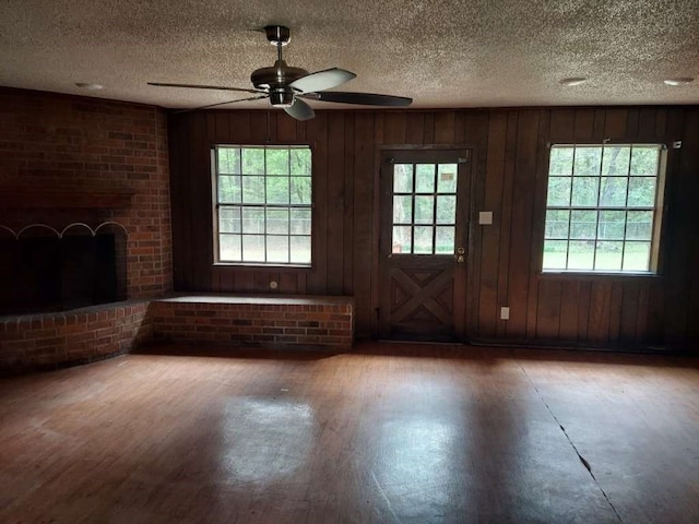 unfurnished living room featuring ceiling fan, hardwood / wood-style flooring, a brick fireplace, brick wall, and wood walls