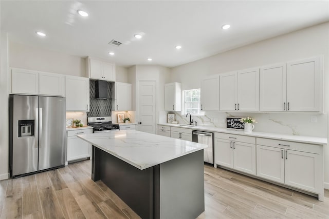 kitchen with sink, white cabinetry, a center island, appliances with stainless steel finishes, and light stone countertops