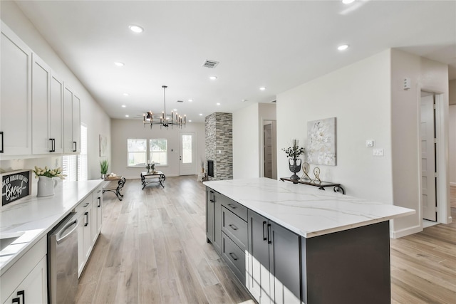 kitchen with hanging light fixtures, white cabinetry, light stone countertops, and dishwasher