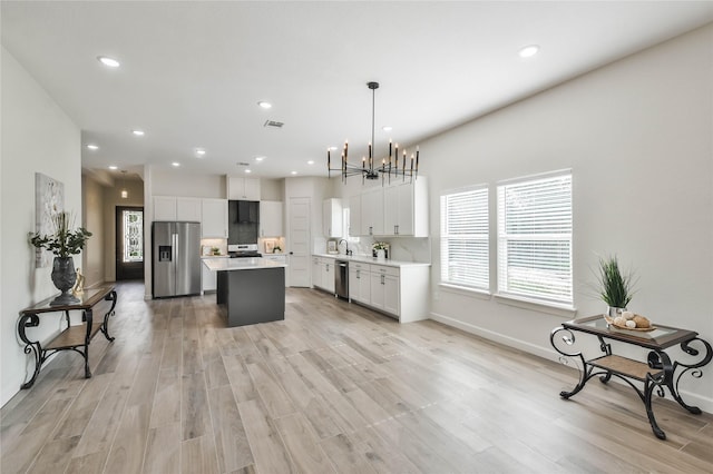 kitchen featuring decorative light fixtures, a center island, light wood-type flooring, stainless steel appliances, and white cabinets