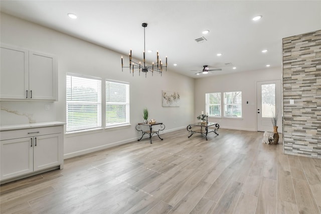 unfurnished room with ceiling fan with notable chandelier and light hardwood / wood-style flooring