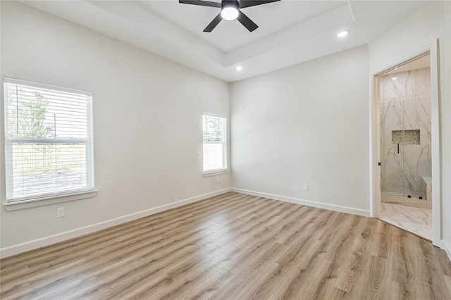 unfurnished bedroom with ceiling fan, connected bathroom, light hardwood / wood-style floors, and a tray ceiling