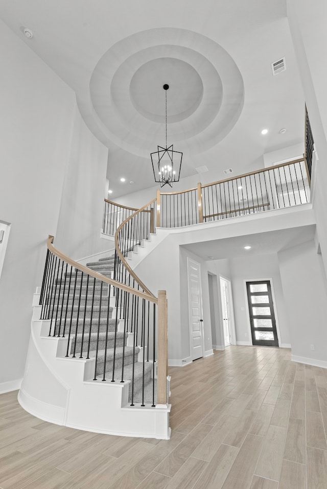 stairs featuring a notable chandelier, light hardwood / wood-style flooring, a tray ceiling, and a high ceiling