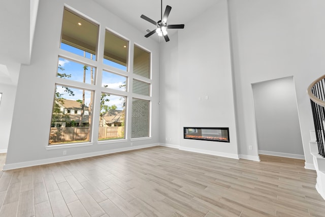 unfurnished living room with ceiling fan, a towering ceiling, and light wood-type flooring