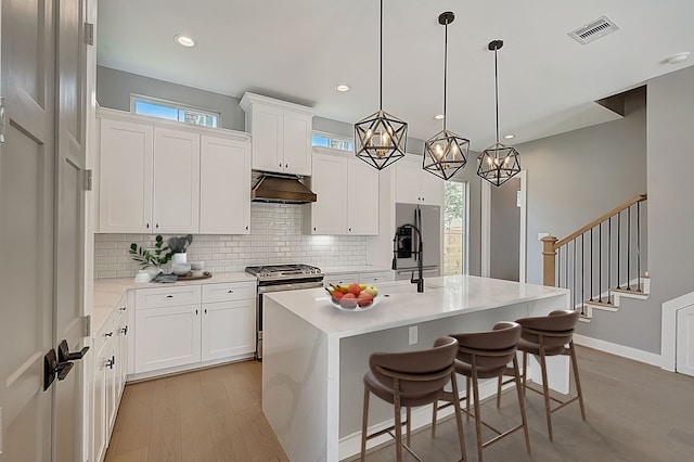 kitchen with a kitchen island with sink, tasteful backsplash, white cabinets, hanging light fixtures, and stainless steel gas stove