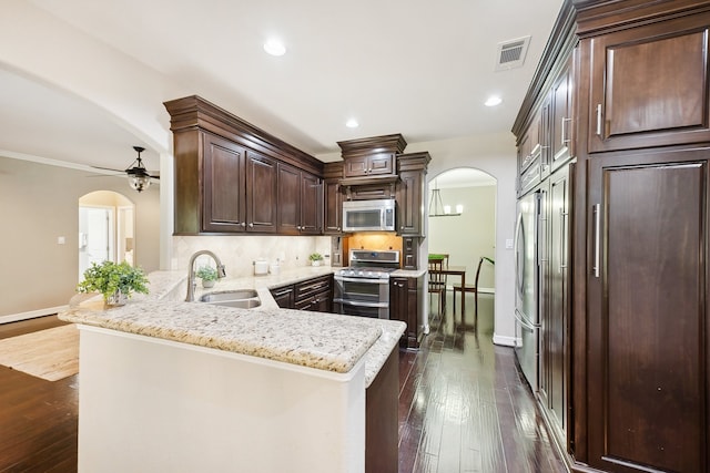 kitchen with ceiling fan, appliances with stainless steel finishes, kitchen peninsula, dark wood-type flooring, and tasteful backsplash