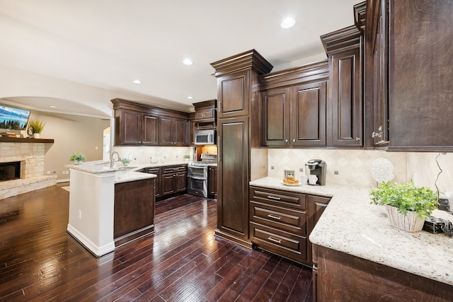 kitchen with tasteful backsplash, a stone fireplace, dark brown cabinets, appliances with stainless steel finishes, and dark wood-type flooring