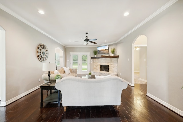 living room featuring a stone fireplace, ornamental molding, dark hardwood / wood-style flooring, and ceiling fan