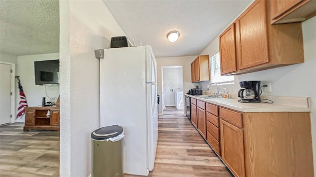 kitchen featuring washer / dryer, a textured ceiling, light hardwood / wood-style floors, white fridge, and sink