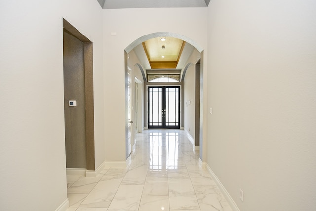 hallway featuring french doors, light tile patterned flooring, and a tray ceiling