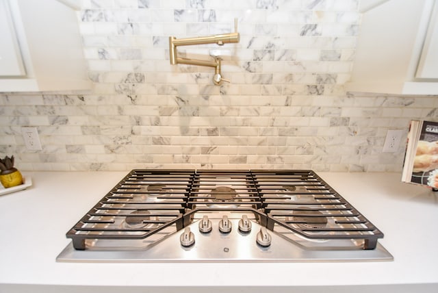 details with stainless steel gas cooktop, white cabinetry, and decorative backsplash