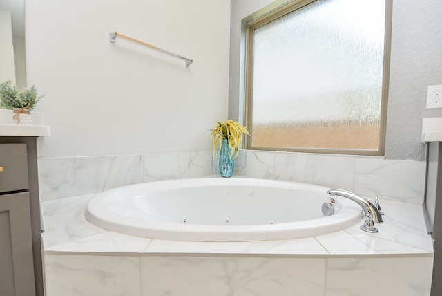 bathroom featuring tiled bath, vanity, and a wealth of natural light