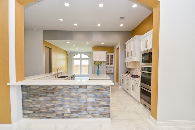 kitchen featuring tasteful backsplash, white cabinetry, kitchen peninsula, stainless steel appliances, and sink