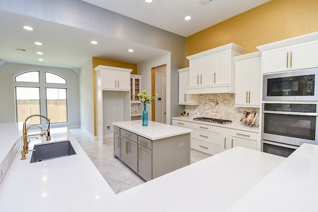 kitchen featuring stainless steel appliances, white cabinets, a kitchen island, sink, and backsplash