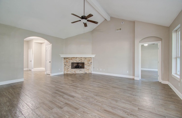 unfurnished living room with light hardwood / wood-style flooring, ceiling fan, high vaulted ceiling, a stone fireplace, and beamed ceiling