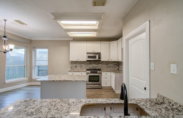 kitchen featuring stainless steel appliances, hanging light fixtures, decorative backsplash, light stone countertops, and wood-type flooring