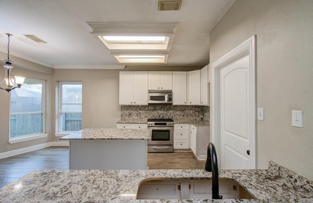 kitchen with appliances with stainless steel finishes, pendant lighting, and light stone counters