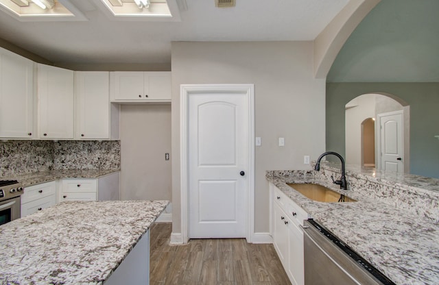 kitchen with light stone counters, white cabinetry, appliances with stainless steel finishes, light hardwood / wood-style floors, and sink