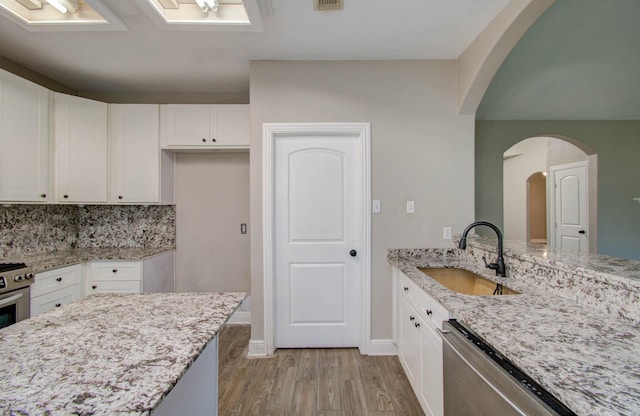 kitchen featuring sink, white cabinetry, light wood-type flooring, dishwashing machine, and light stone countertops