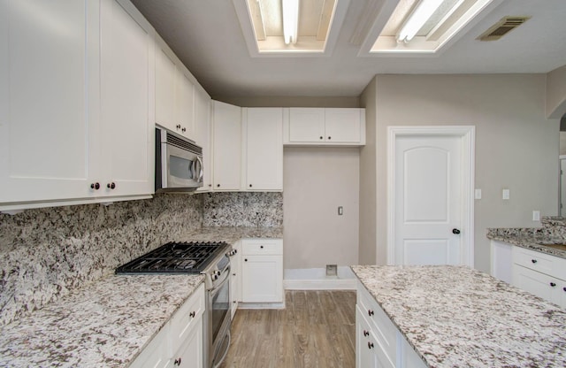 kitchen with light wood-type flooring, stainless steel appliances, white cabinetry, backsplash, and light stone counters