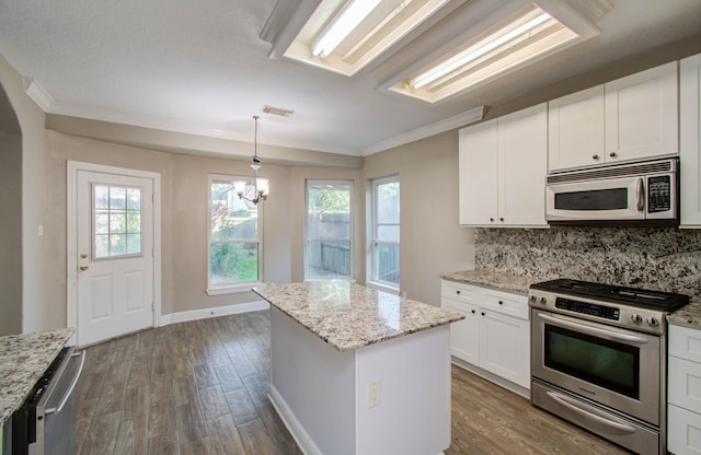 kitchen with a kitchen island, appliances with stainless steel finishes, pendant lighting, white cabinets, and light stone countertops