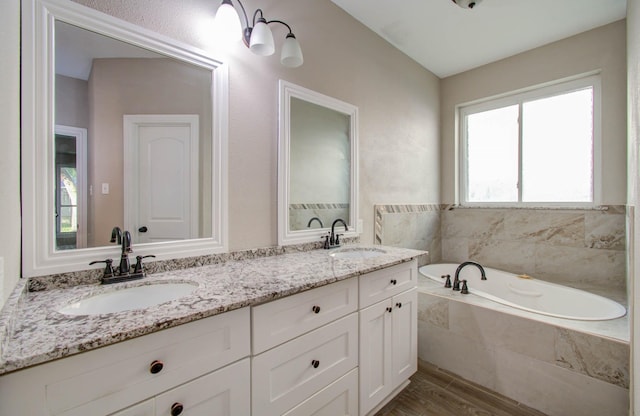 bathroom with hardwood / wood-style flooring, vanity, and a relaxing tiled tub