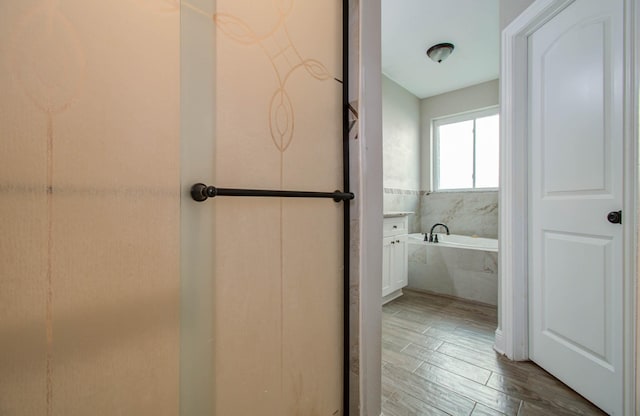 bathroom featuring vanity, tiled tub, and wood-type flooring