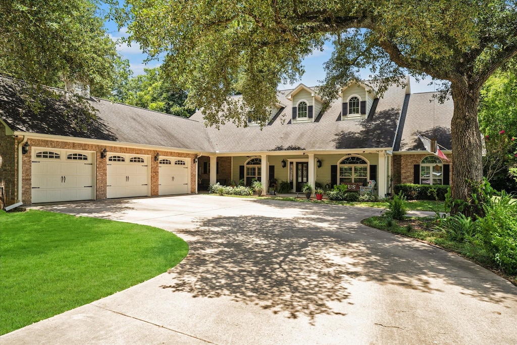 cape cod home with a garage, a front yard, brick siding, and driveway