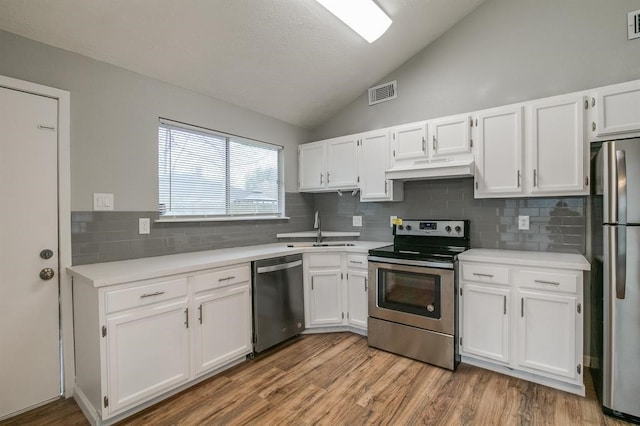 kitchen featuring stainless steel appliances, vaulted ceiling, light wood-type flooring, tasteful backsplash, and sink