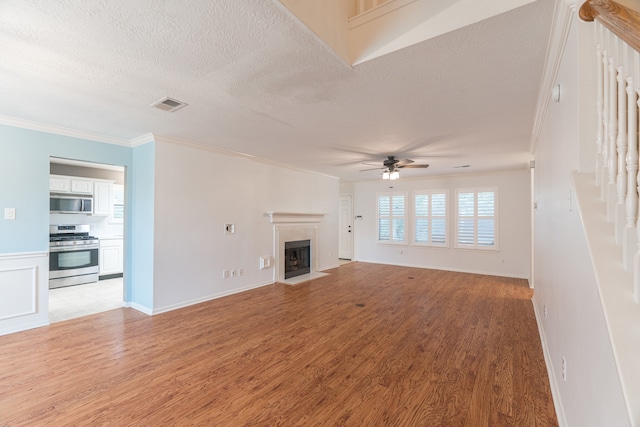 unfurnished living room featuring ceiling fan, light wood-type flooring, ornamental molding, and a textured ceiling