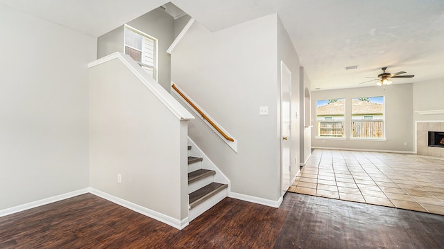 stairs with a tiled fireplace, wood-type flooring, and ceiling fan