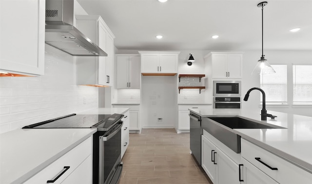 kitchen with sink, white cabinetry, pendant lighting, stainless steel appliances, and wall chimney range hood