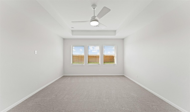 empty room featuring ceiling fan, a raised ceiling, and light carpet