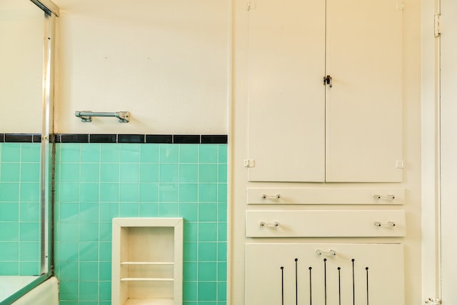 bathroom with tile walls and combined bath / shower with glass door