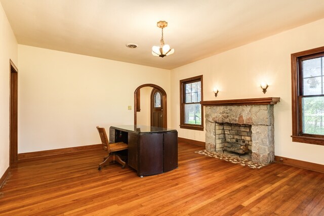 dining space featuring wood-type flooring, a chandelier, a stone fireplace, and a healthy amount of sunlight