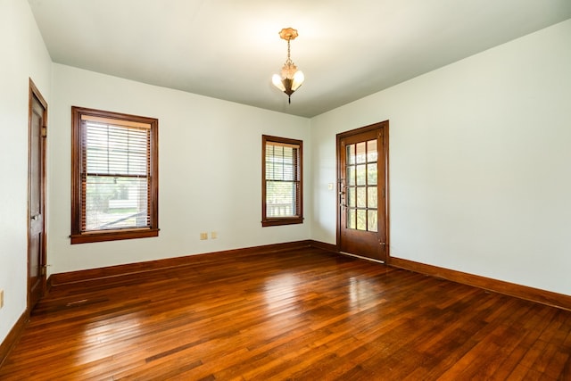 spare room featuring wood-type flooring, a chandelier, and a healthy amount of sunlight