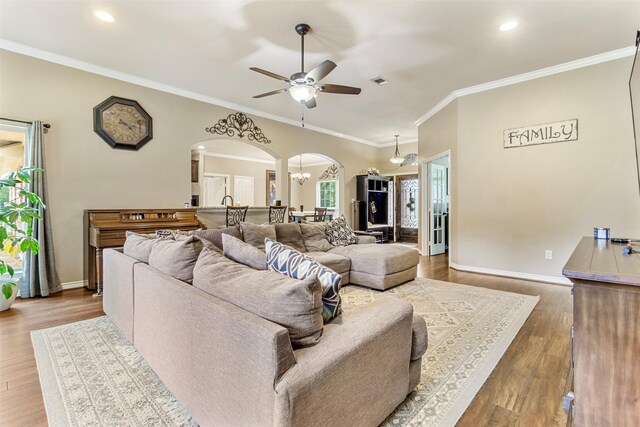 living room featuring light wood-type flooring, ornamental molding, and ceiling fan with notable chandelier