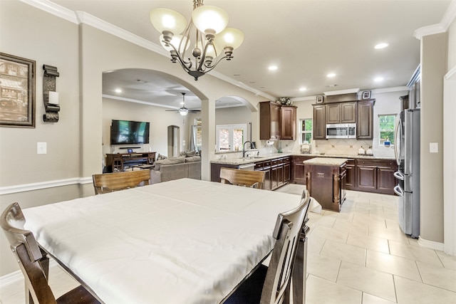 tiled dining area featuring sink, ornamental molding, ceiling fan with notable chandelier, and plenty of natural light