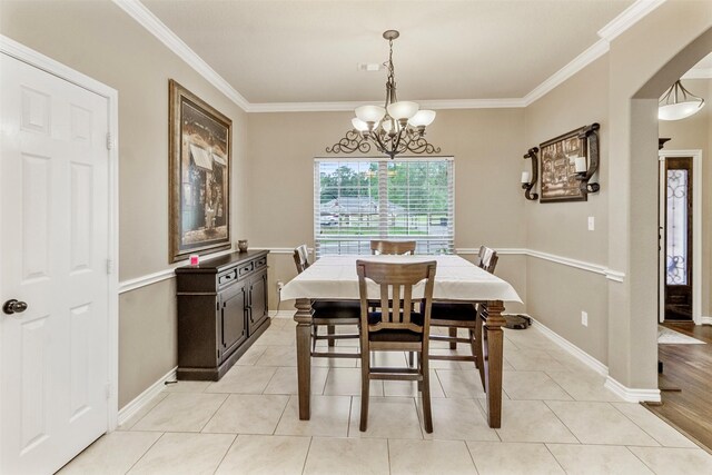 tiled dining room with ornamental molding and a chandelier