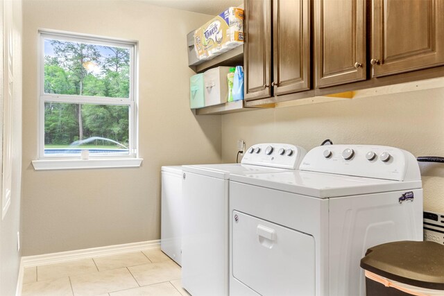 clothes washing area featuring washing machine and dryer, light tile patterned flooring, cabinets, and a healthy amount of sunlight