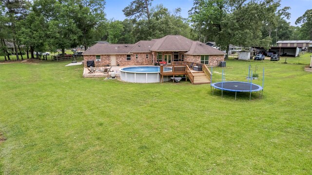 rear view of property with a lawn, a swimming pool side deck, a trampoline, and an outbuilding